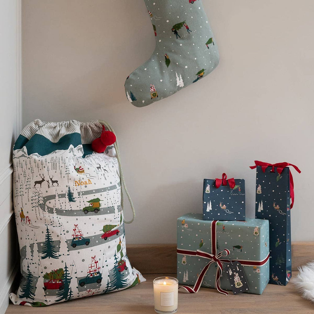Christmas-themed gift bag, stocking, and wrapped presents on a wooden surface.