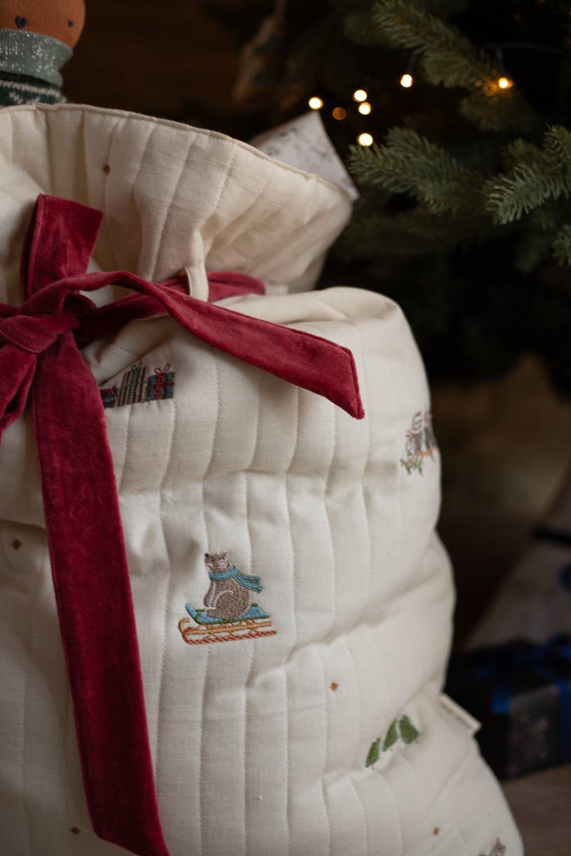 White quilted bag with red ribbon and embroidered design, Christmas tree in the background