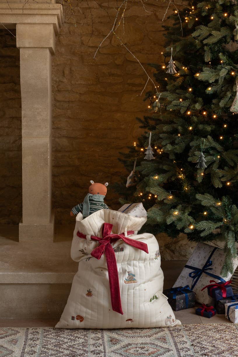White gift bag with a red ribbon in front of a decorated Christmas tree.