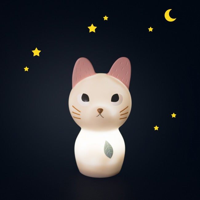 Cream cat-shaped night light with pink ears and a blue leaf detail glowing softly against a dark navy background with yellow stars and a crescent moon.
