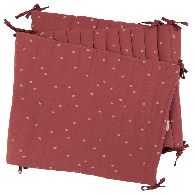 Terracotta After the Rain cot bumper fitted around a cot, showing its quilted panels, gold leaf details and tie fastenings