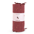 Terracotta After the Rain cot bumper with small gold leaf details and tie fastenings, rolled in Moulin Roty packaging on a white background