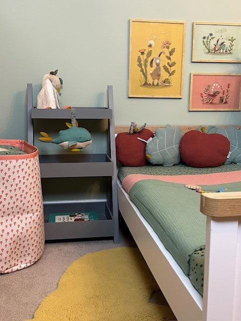 Apple-shaped plum cushion displayed on a child’s bed alongside a turquoise leaf cushion in a colourful bedroom