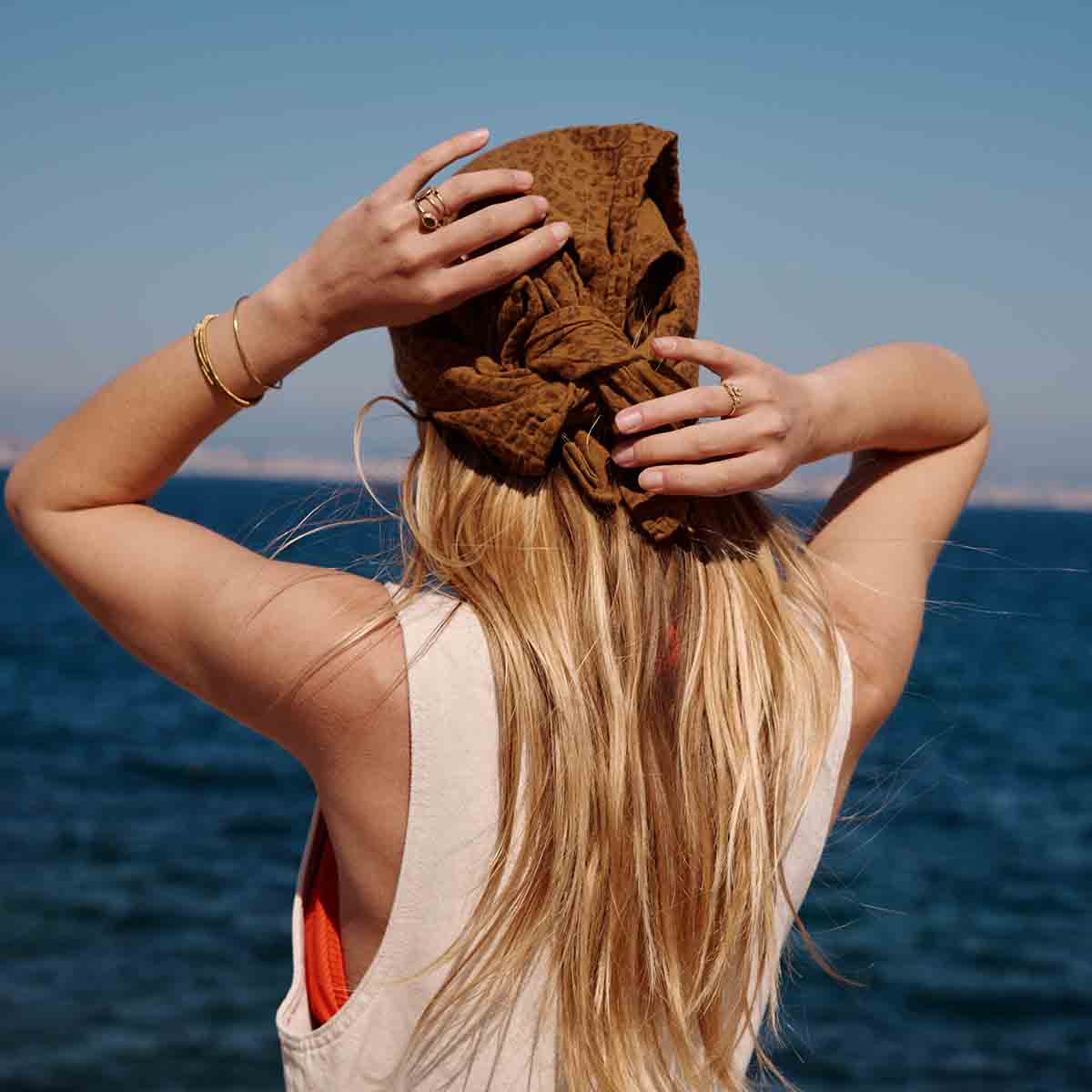 Rear view of a woman wearing the brown leopard-print scarf tied at the back of her head beside the sea.