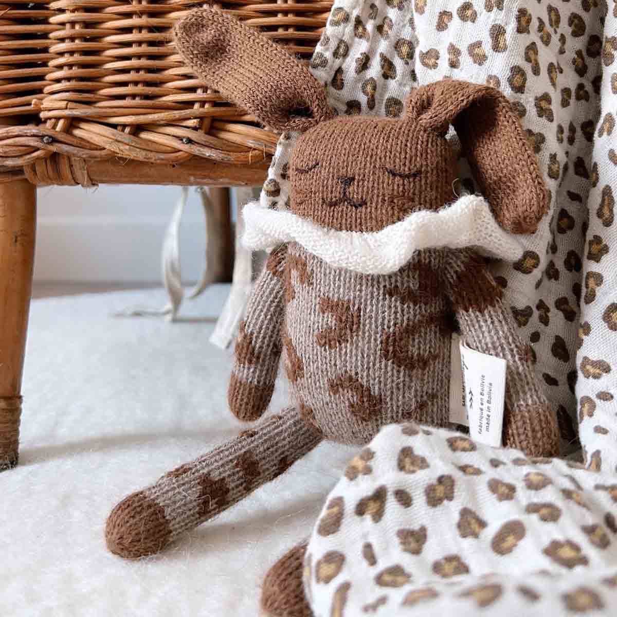 Brown knitted rabbit soft toy resting against a Bianca Mini Leopard Greige muslin swaddle, highlighting the coordinating neutral and brown tones.