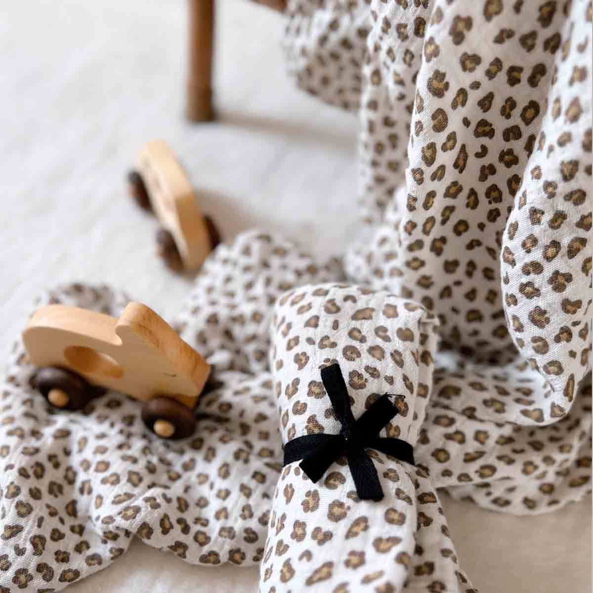 Bianca Mini Leopard Greige muslin swaddle arranged with small wooden toy cars, with a second swaddle rolled and tied with a black ribbon.