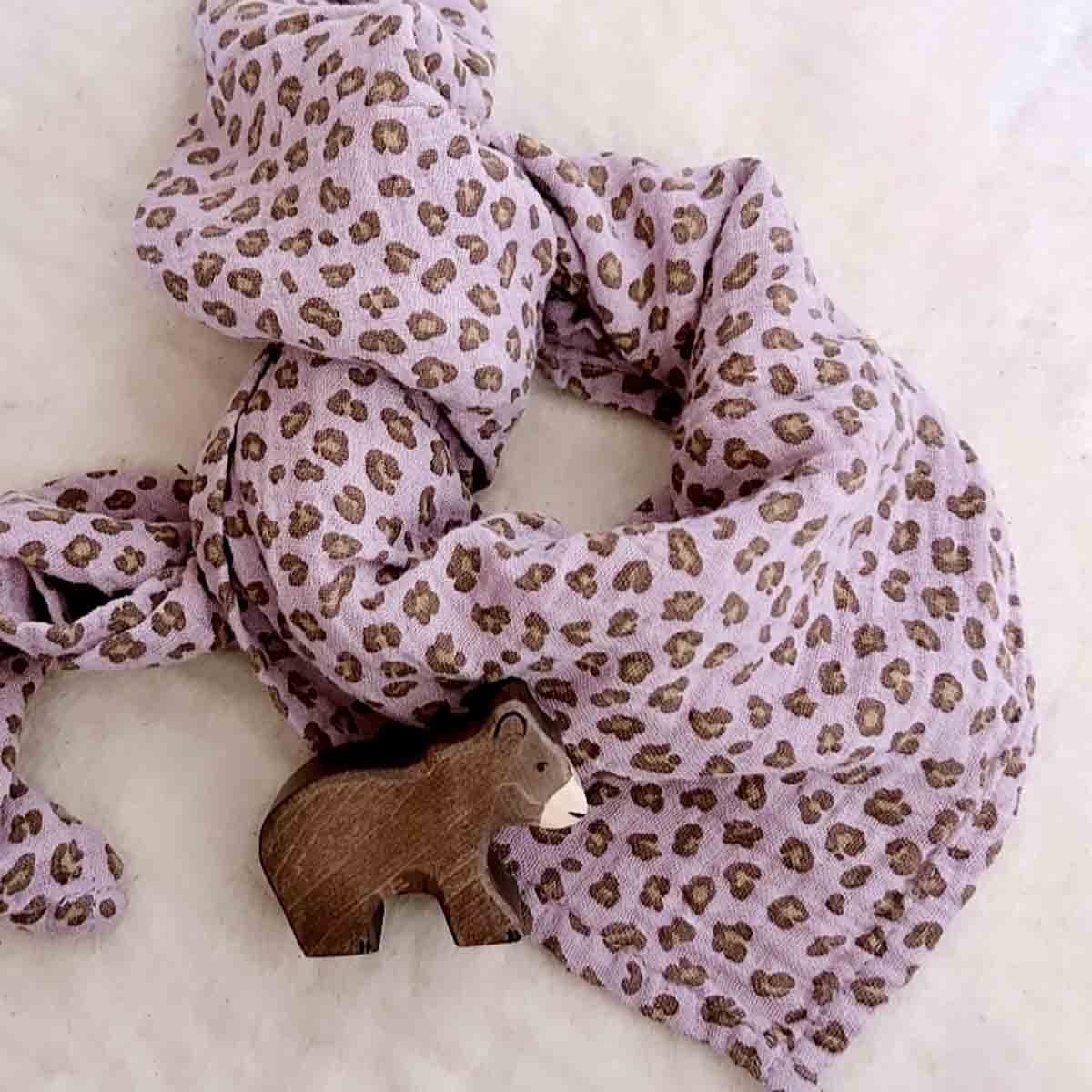 Close-up of lilac cotton muslin fabric with a brown leopard print arranged beside a small wooden animal toy.