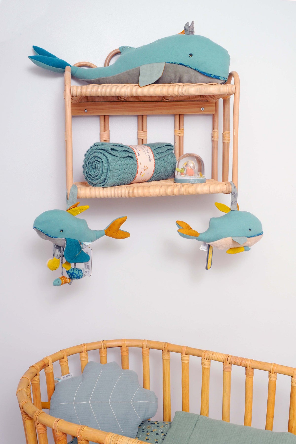Blue whale cushion displayed on a rattan nursery shelf above a cot, with matching whale decorations and a green knitted blanket