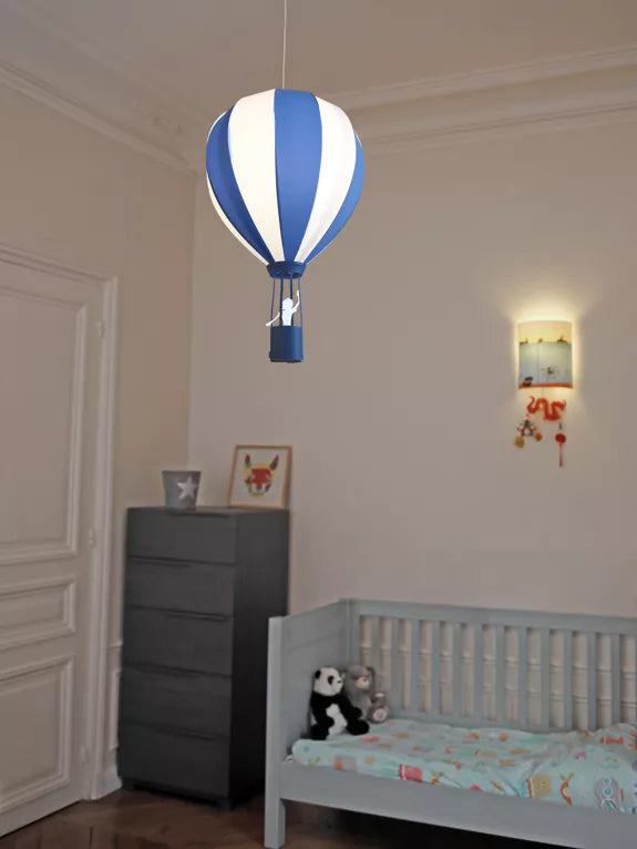 Blue and white striped hot air balloon pendant light hanging above a child’s cot in a nursery