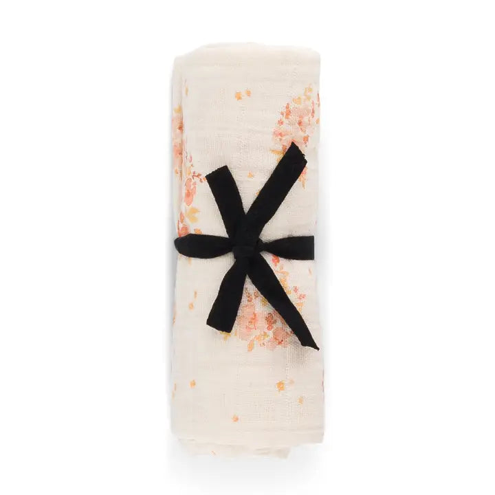 Folded cream muslin blanket with delicate peach bouquet prints, tied with a black ribbon against a white background.