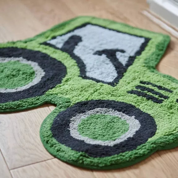 Close-up of a bright green tractor-shaped rug showing its textured surface, black wheels and grey cab on a wooden floor