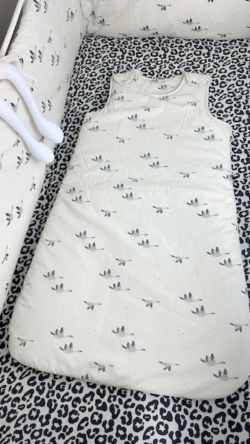 Charly Goose baby sleeping bag in cream with a grey flying goose print, laid flat inside a cot with a black and cream Graou animal print fitted sheet.
