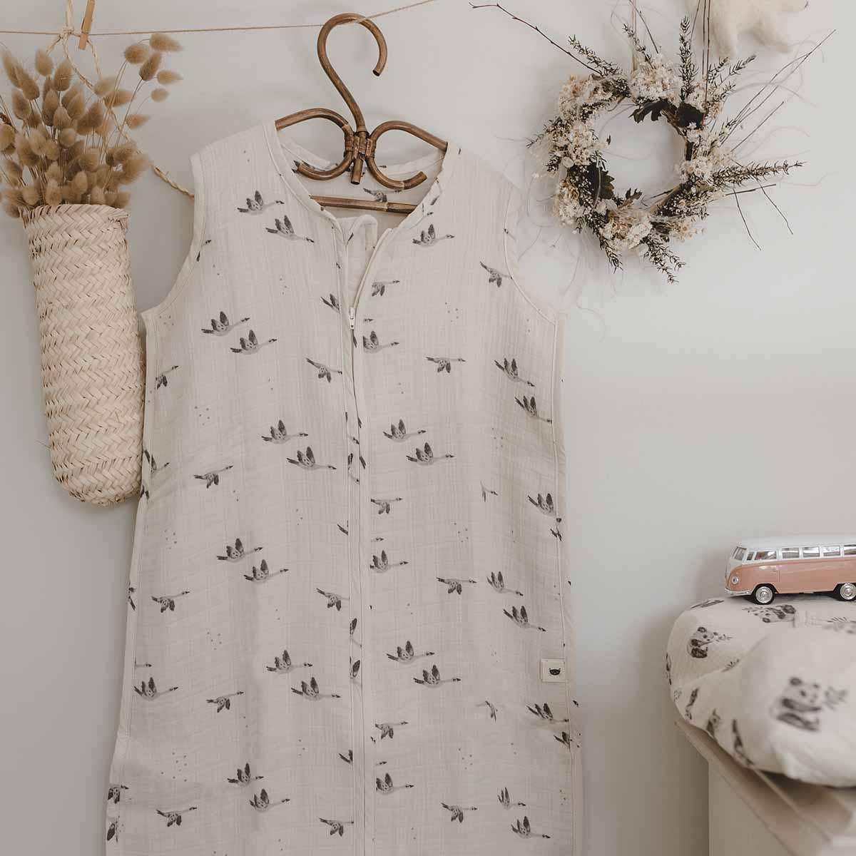 Charly Goose lightweight summer baby sleeping bag in cream with a grey flying goose print and front zip, displayed on a wooden hanger in a neutral nursery setting.