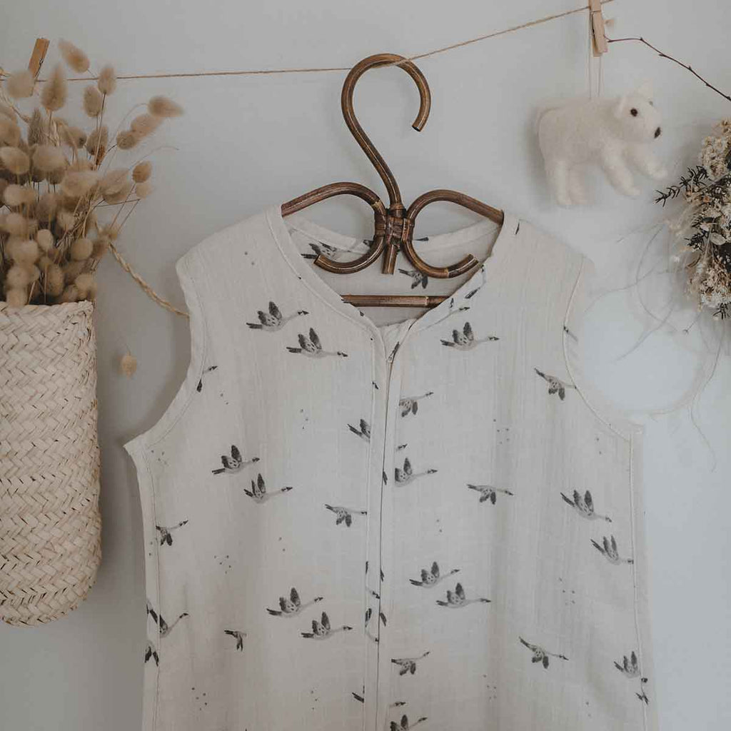 Charly Goose lightweight summer baby sleeping bag in cream with a grey flying goose print and front zip, hanging on a wooden hanger in a neutral nursery setting.