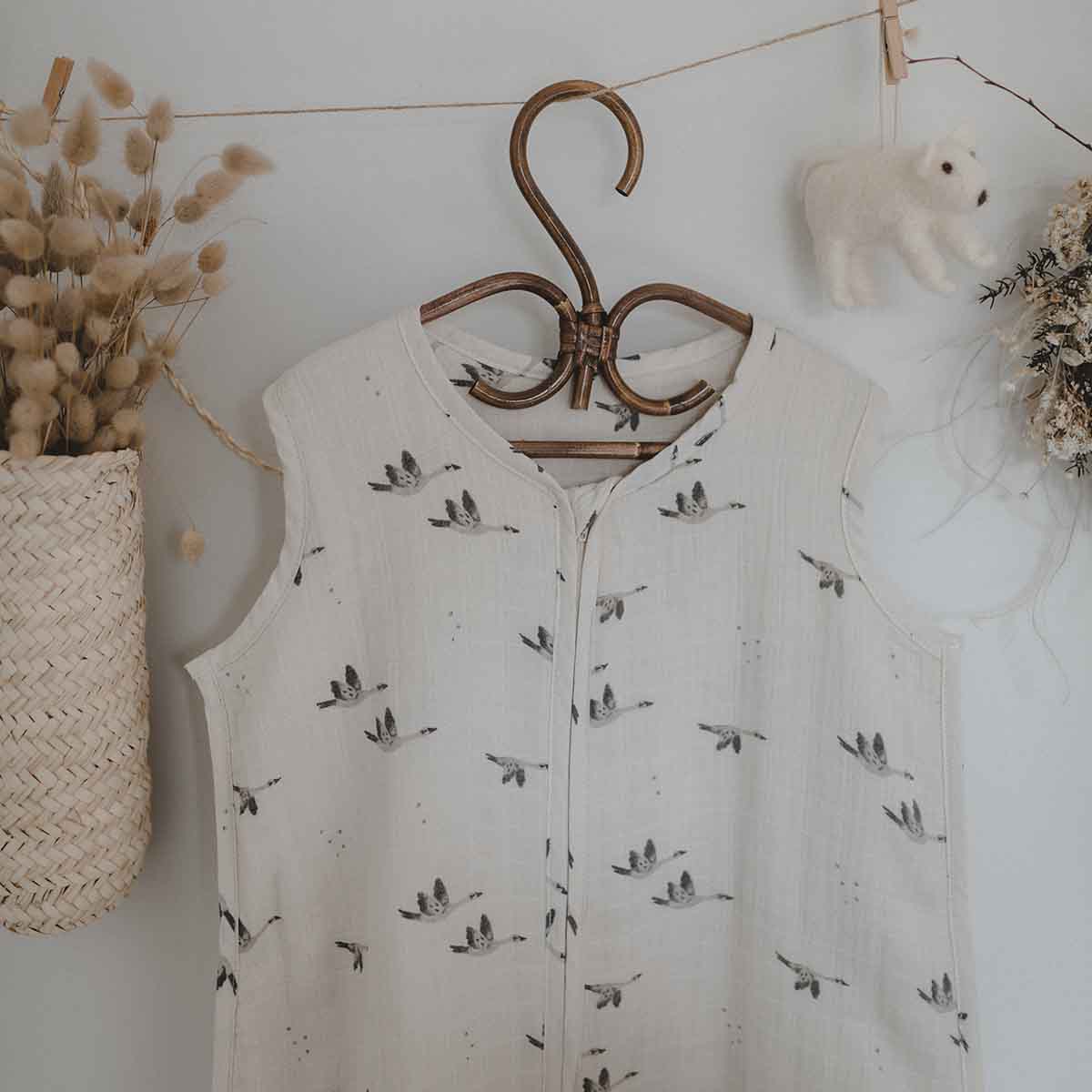 Charly Goose lightweight summer baby sleeping bag in cream with a grey flying goose print and front zip, hanging on a wooden hanger in a neutral nursery setting.