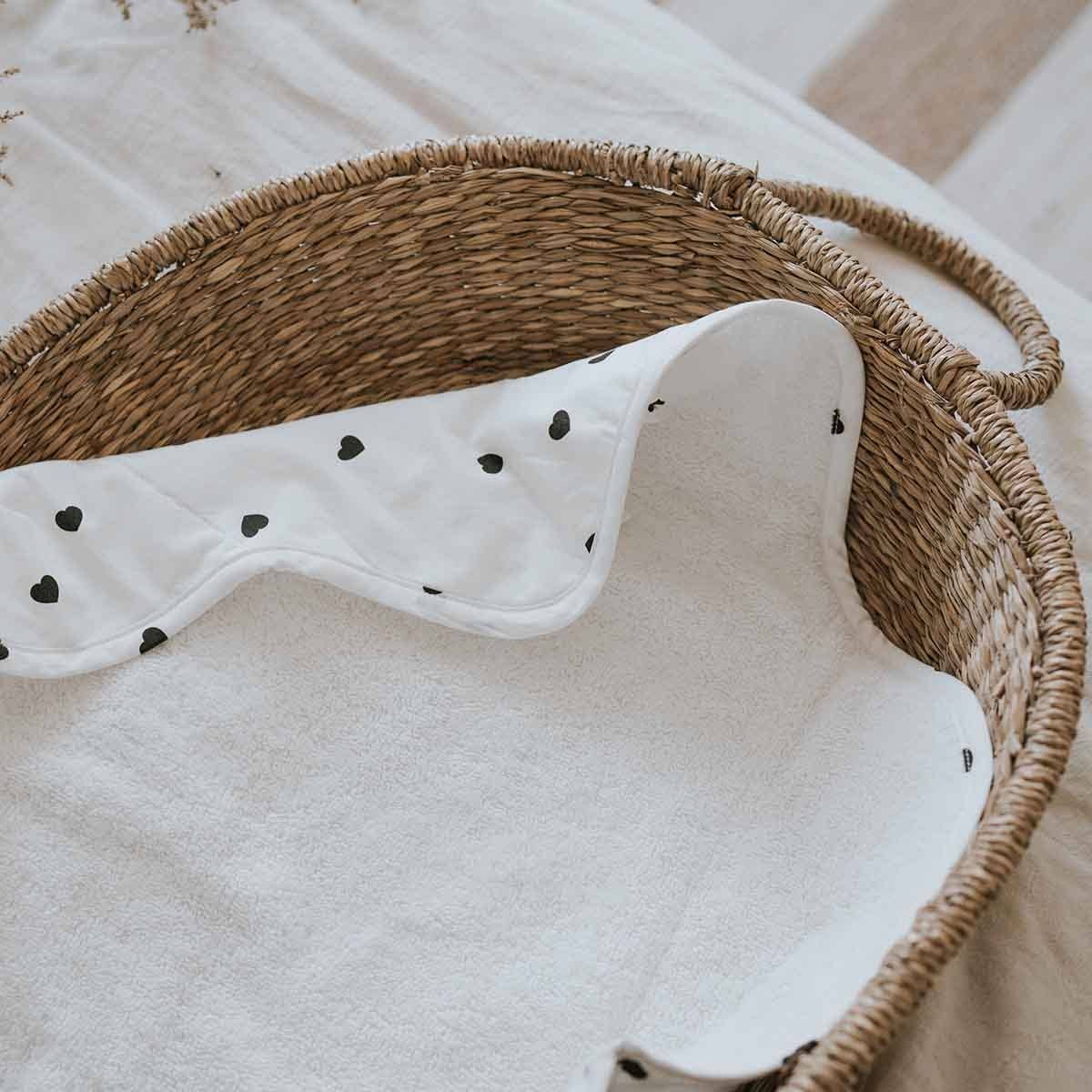 Open Charly Nomad changing mat with a black heart print outer fabric and soft white terry lining, displayed in a woven basket.