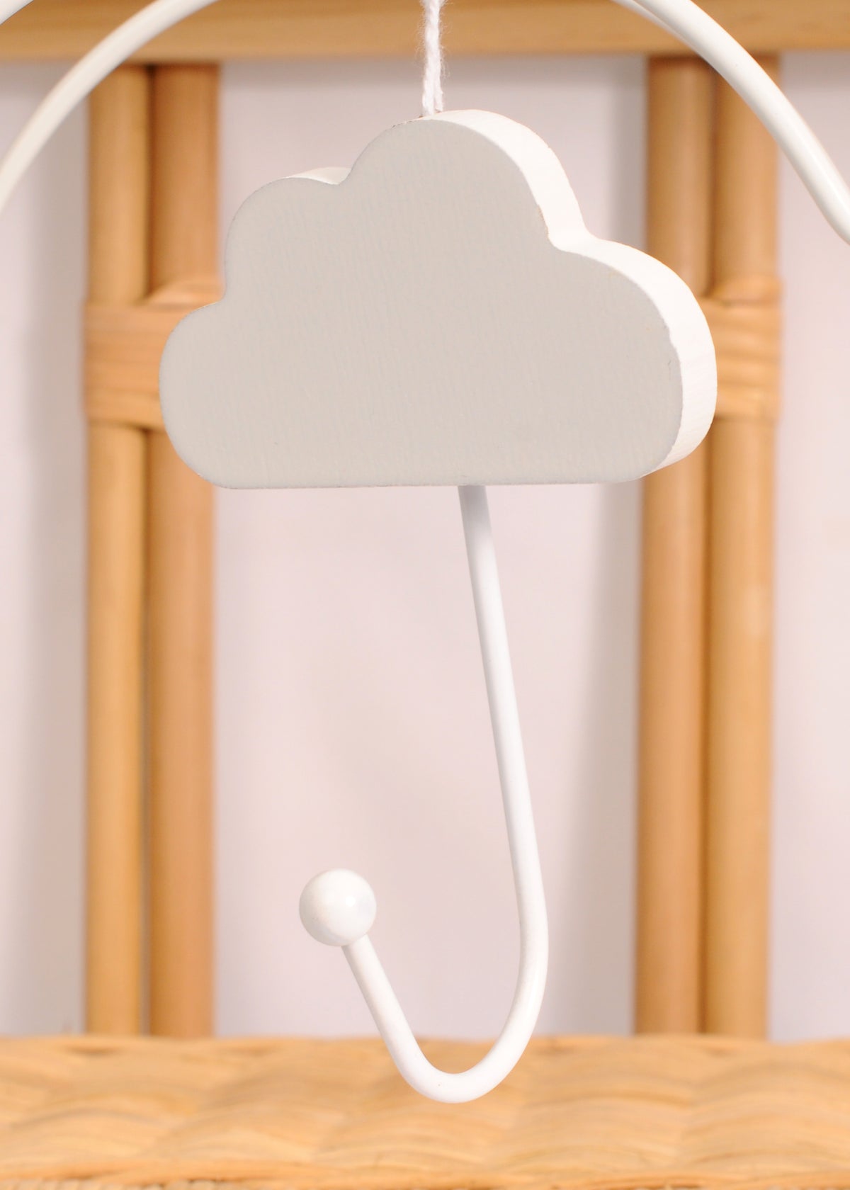 White cloud-shaped wall hook hanging against a wooden nursery backdrop with a curved hook and round end