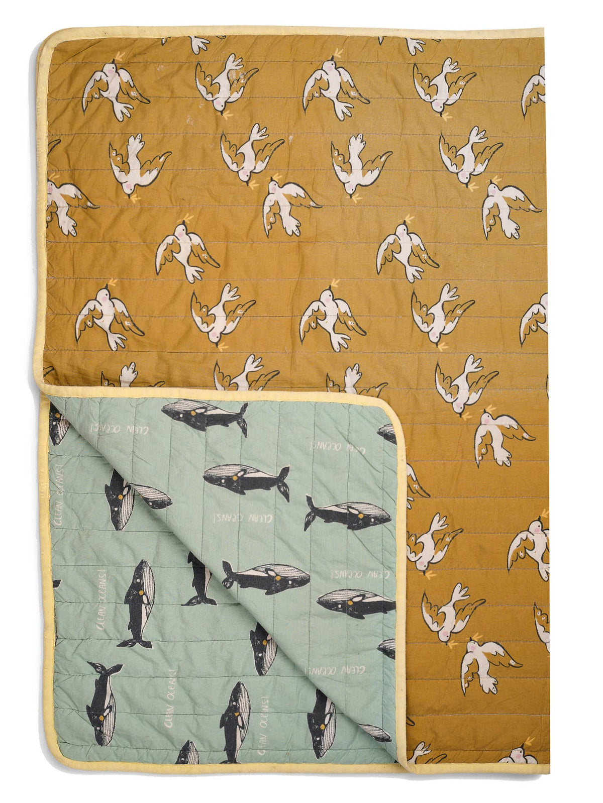 Reversible quilt featuring a mustard background with white bird prints on one side and a sage green background with black whale prints on the other, finished with pale yellow edging.
