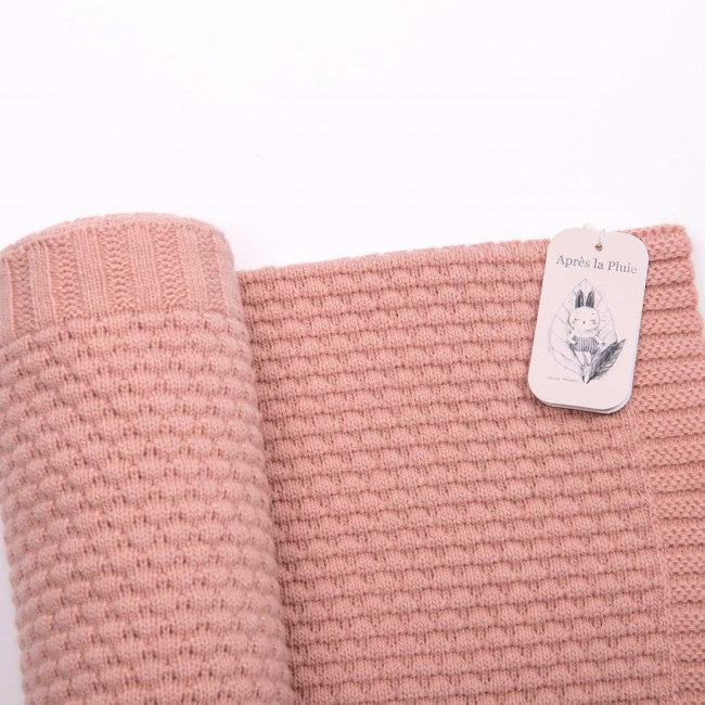 Close-up of a dusky pink wool blend knitted baby blanket showing its textured knit pattern and Moulin Roty label
