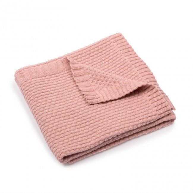 Dusky pink wool blend knitted baby blanket folded on a white background, showing its textured knit pattern and ribbed edging