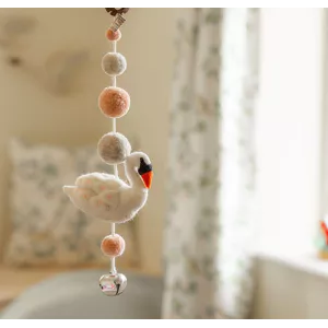 Felt swan garland with pink and neutral pom-poms and a silver bell hanging in a nursery