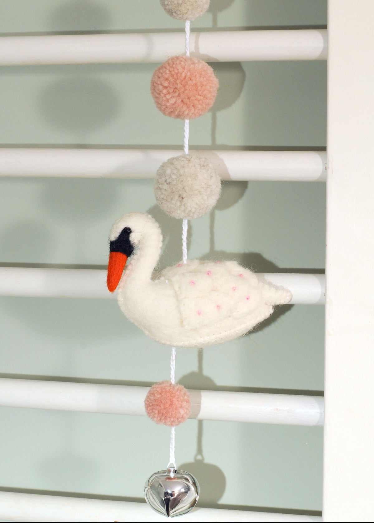 White felt swan garland with pink and cream pom-poms and a silver bell hanging on a white rail