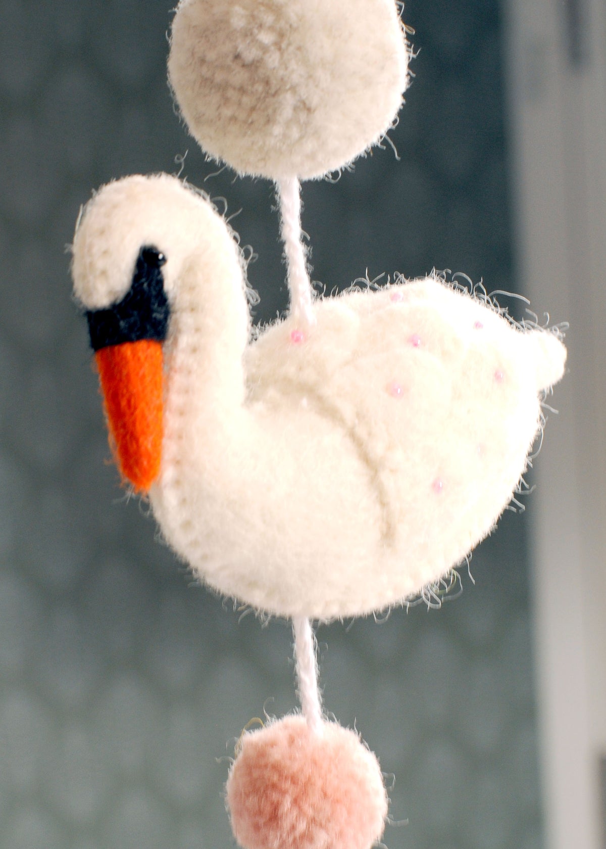 Close-up of a white felt swan with pink details and cream and pink pom-poms