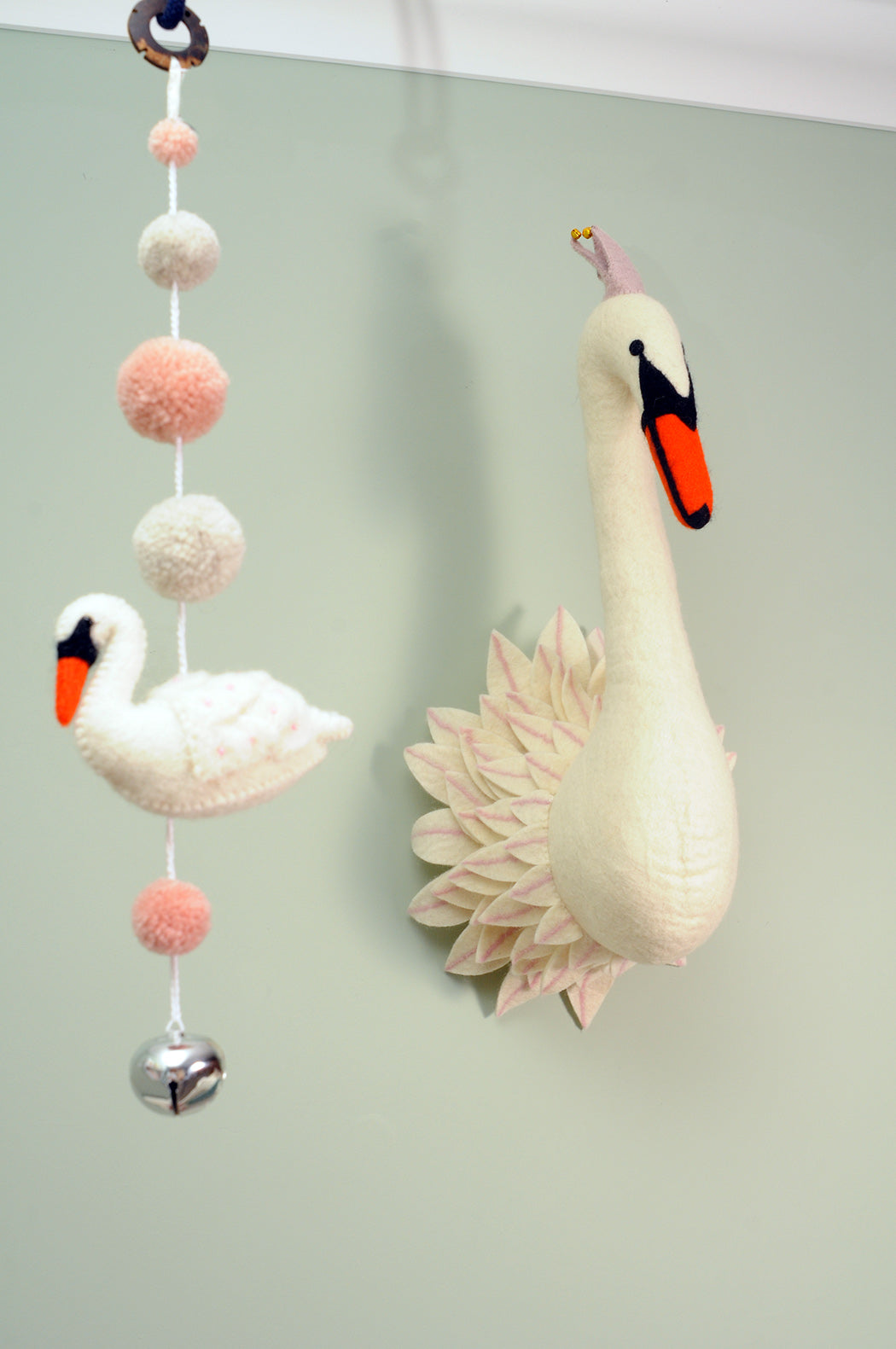 White felt swan wall décor with pink feather details displayed beside a hanging swan decoration