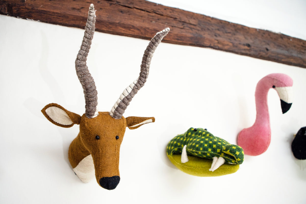Fiona Walker mini green alligator head wall décor displayed alongside a brown antelope head and pink flamingo head on a white wall with a rustic wooden beam.