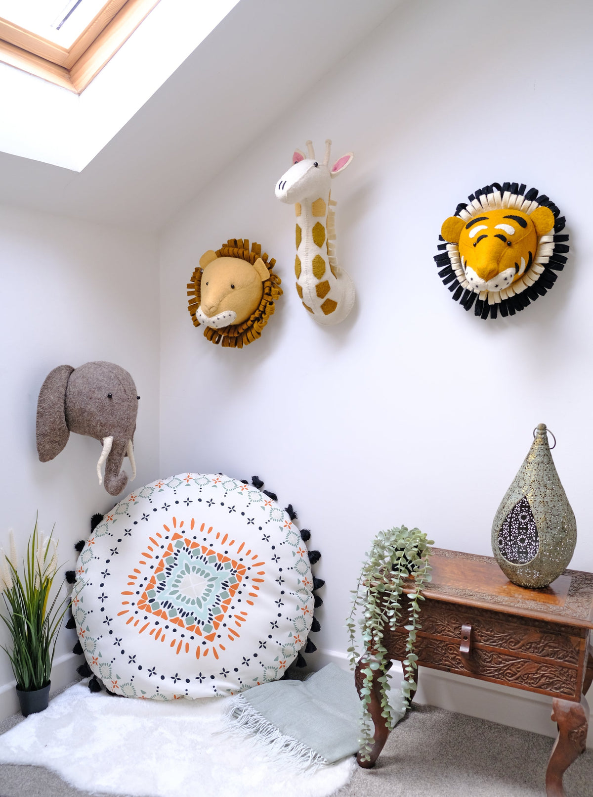 Fiona Walker Roary the Tiger felt wall head displayed alongside a lion, giraffe and elephant wall heads in a safari-themed nursery with a patterned floor cushion and wooden table.