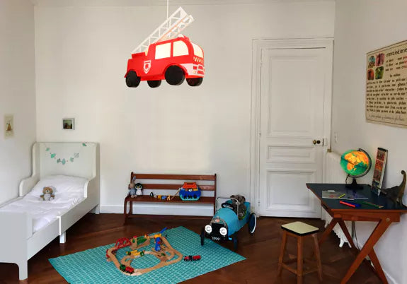 Red fire engine pendant light hanging in a child’s bedroom with a bed, play area and desk