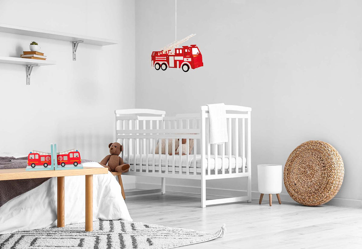 Red fire engine pendant light hanging above a white cot in a nursery with matching fire engine décor