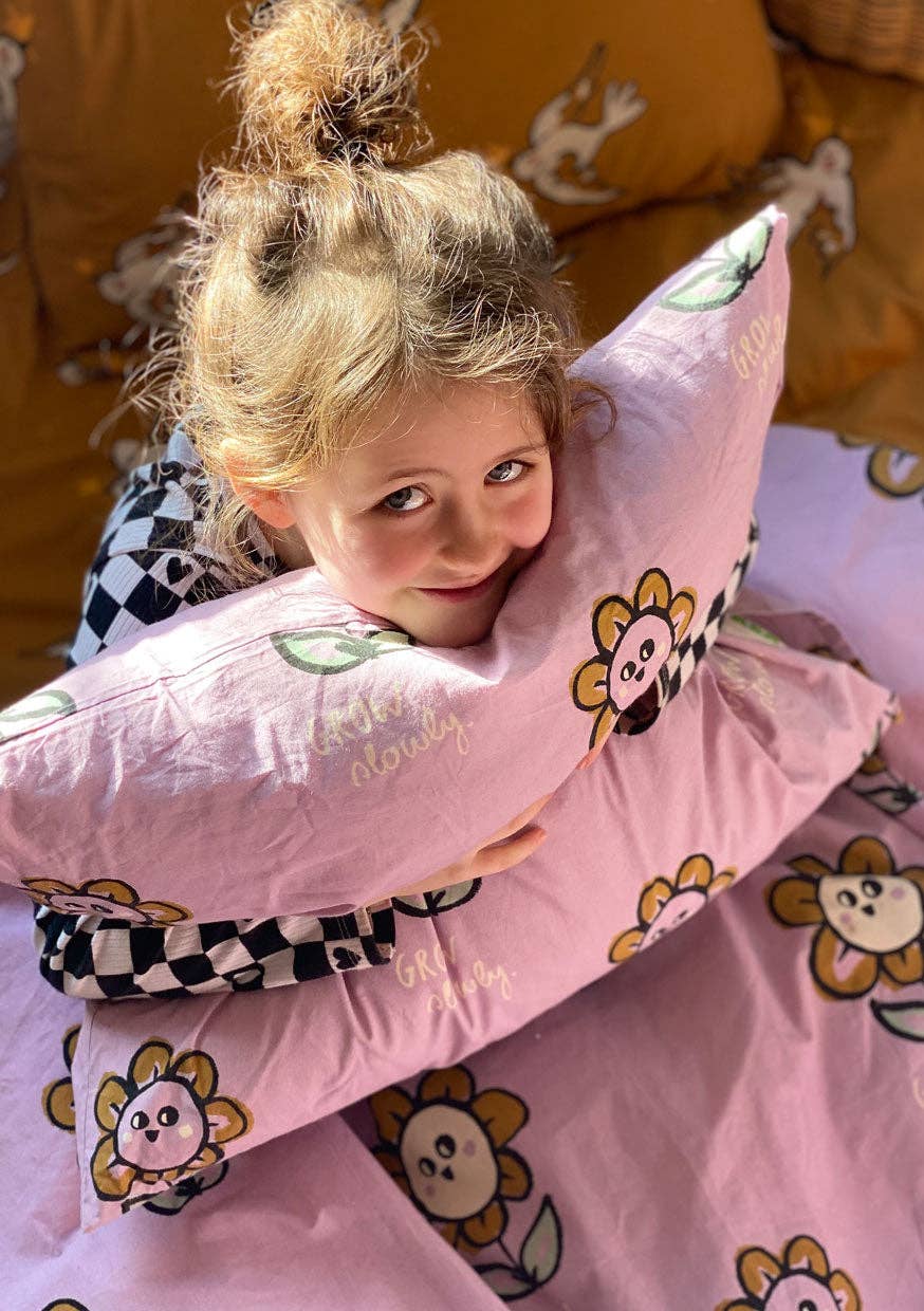 Child cuddling a pink floral duvet cover featuring playful yellow flower characters, green leaves and decorative lettering.