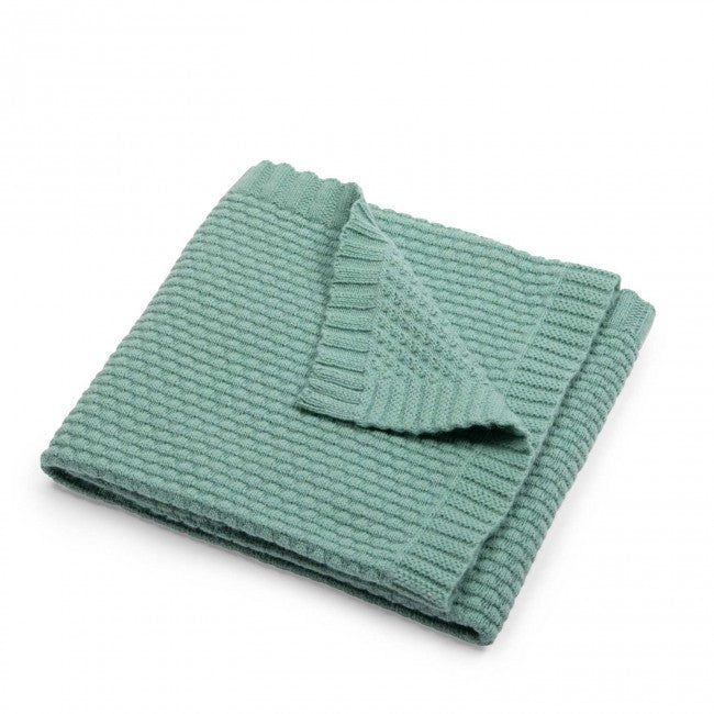 Green wool blend knitted baby blanket folded to show its textured knit pattern and ribbed edging on a white background