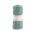 Green wool blend knitted baby blanket rolled and displayed in its Moulin Roty packaging on a white background