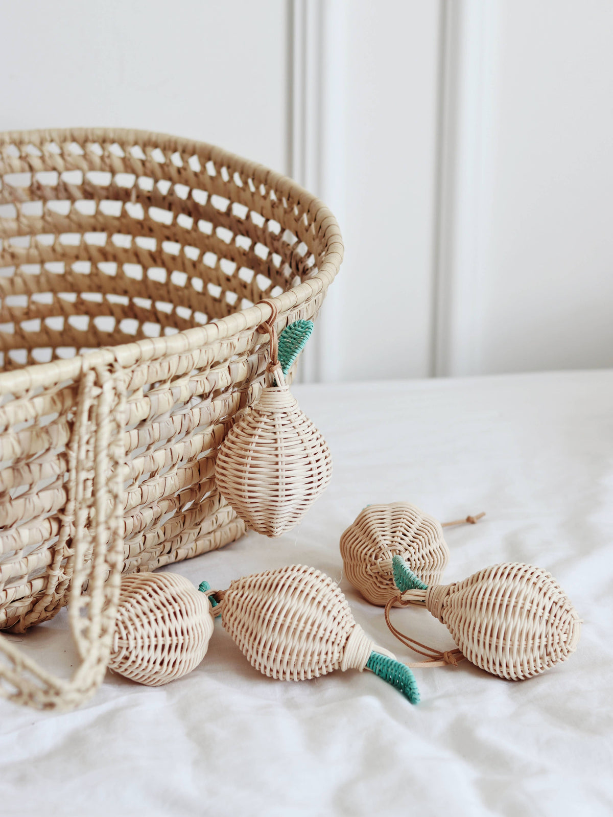 Handmade natural rattan lemon-shaped rattles with woven textures, green woven leaf details and tan leather strings, displayed beside a woven rattan basket.