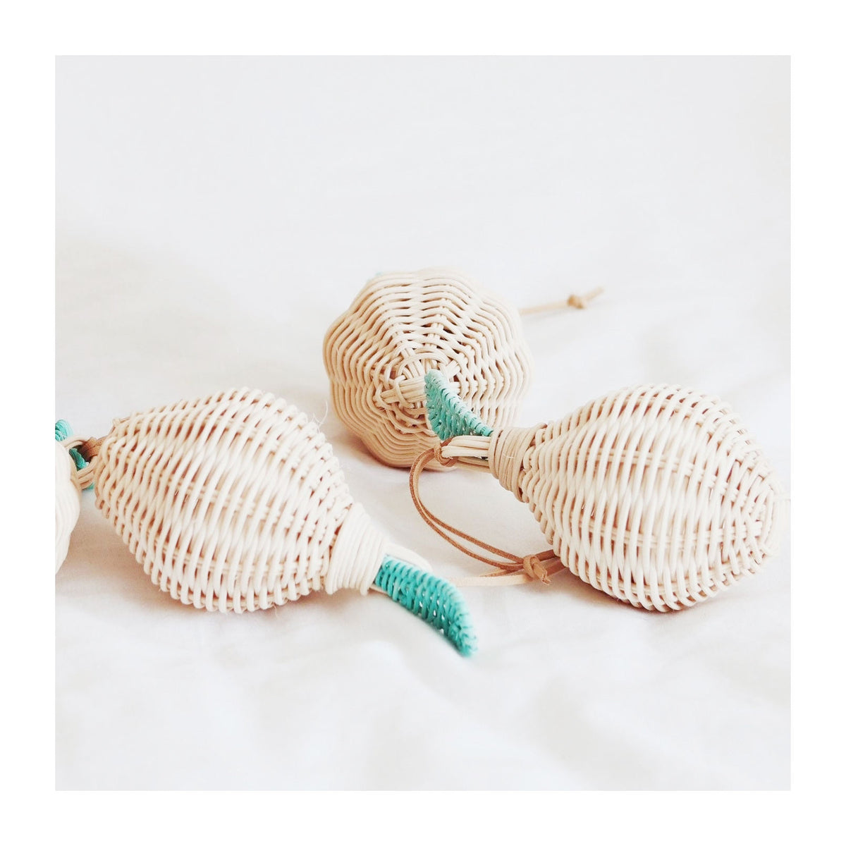 Three handmade woven rattan lemon-shaped rattles with green leaf details and tan leather strings, arranged on a white background.
