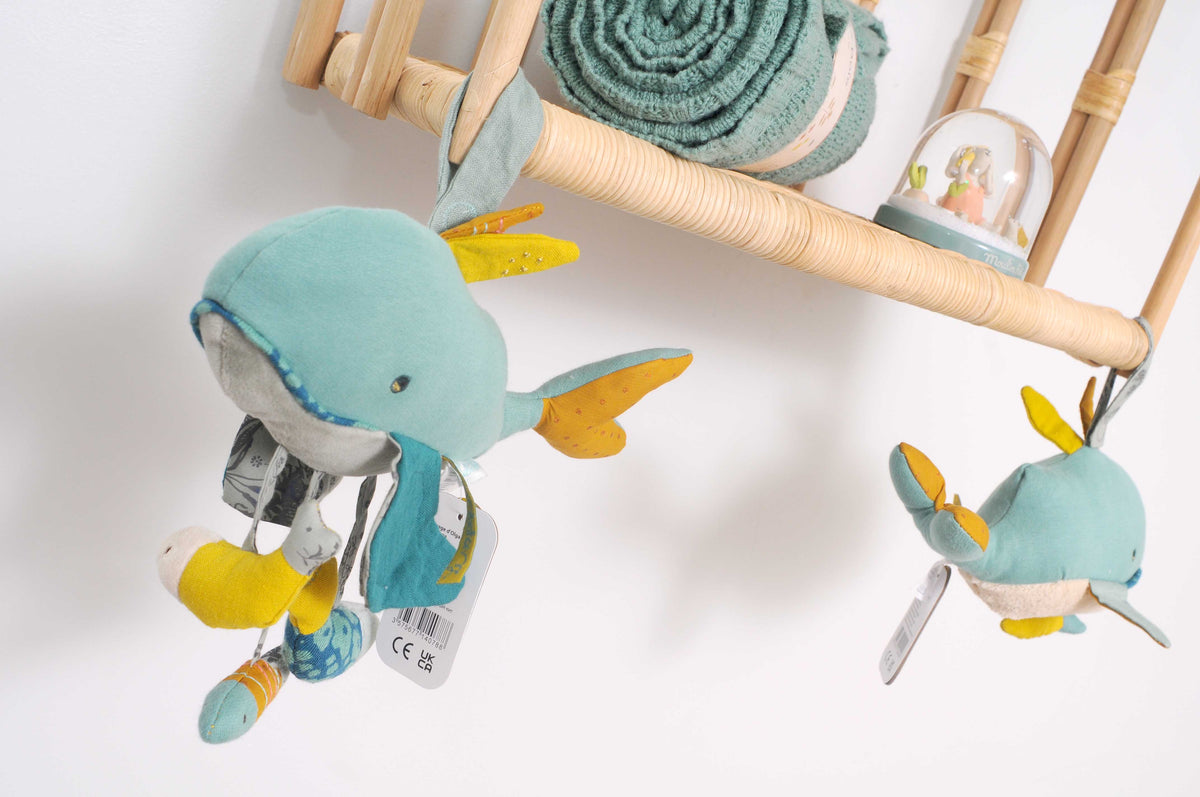 Josephine the sensory blue whale toy hanging in a nursery with a smaller whale toy and knitted blanket nearby