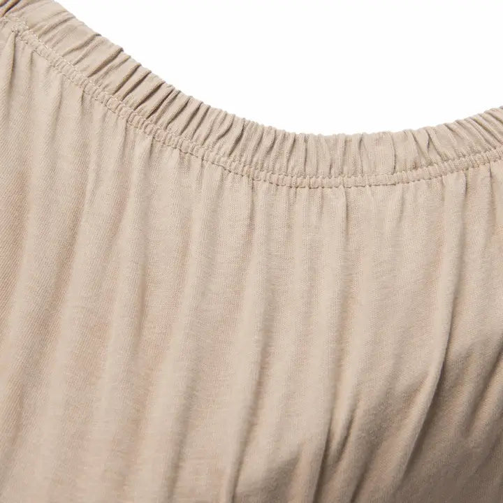 Close-up of a latte-coloured fitted cot sheet showing its soft cotton texture and gathered elasticated edge.