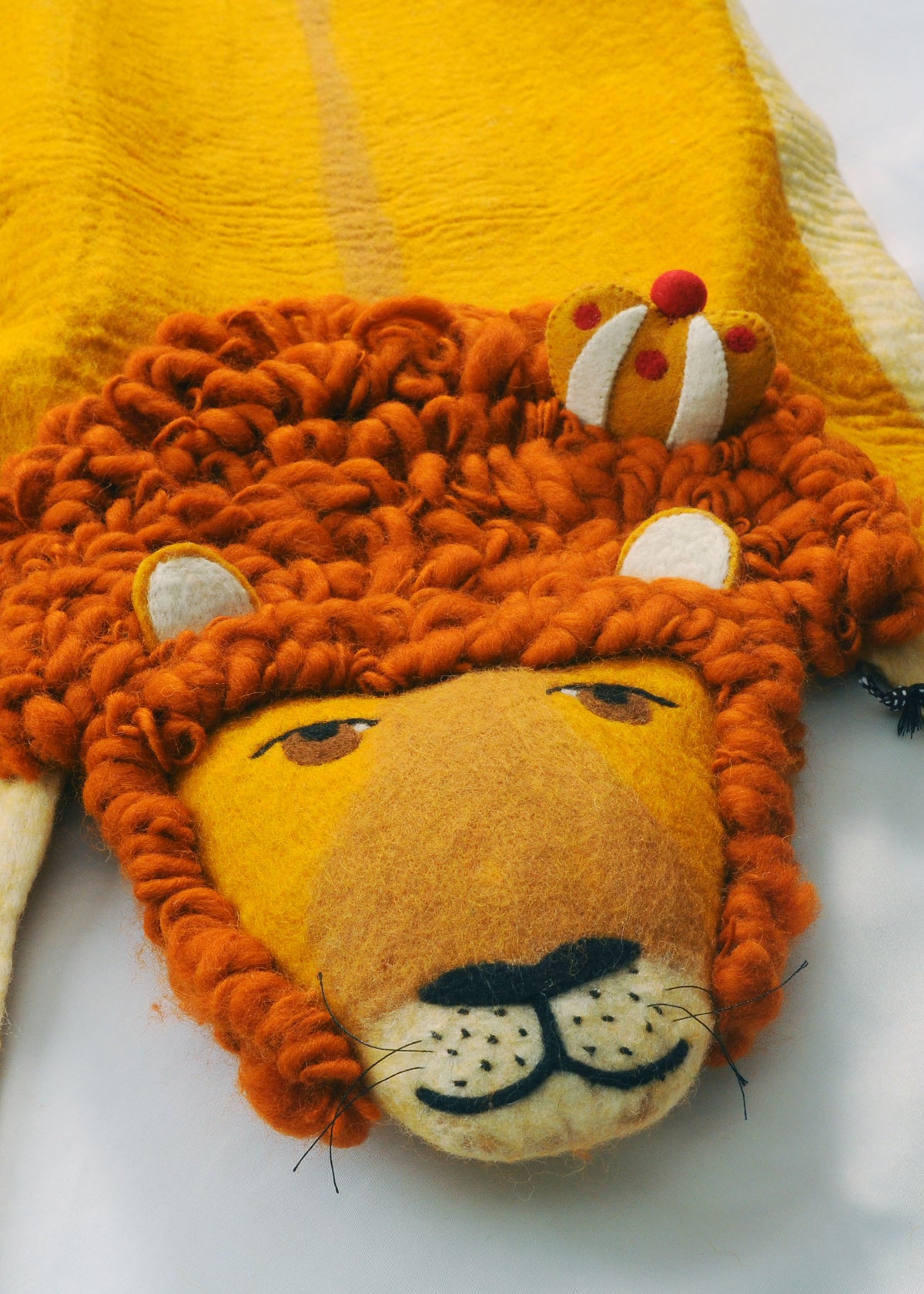 Close-up of a handmade felt lion rug showing its soft brown mane, yellow face, whiskers and decorative crown