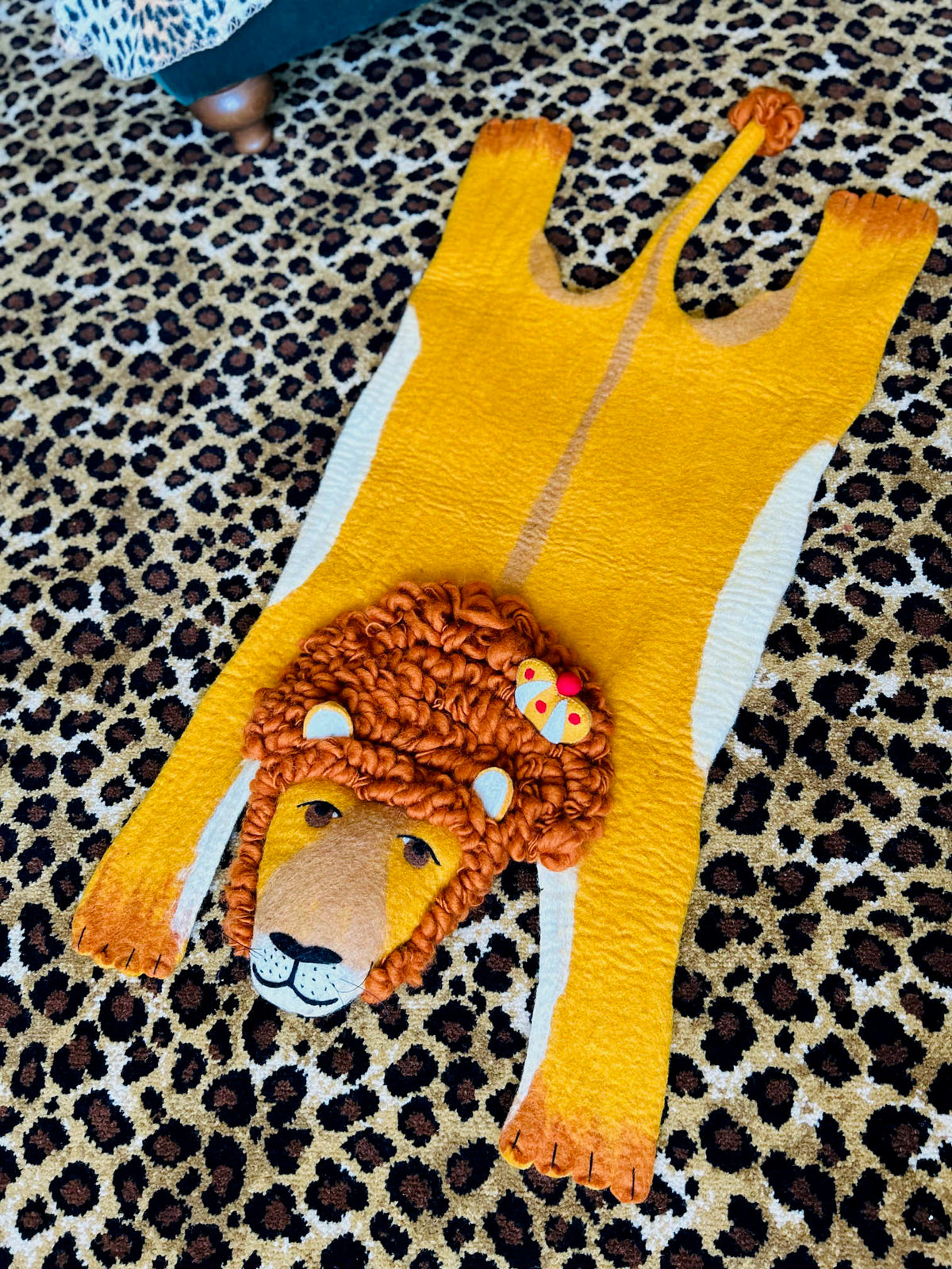 Handmade yellow felt lion rug with a brown mane displayed on a leopard-print rug