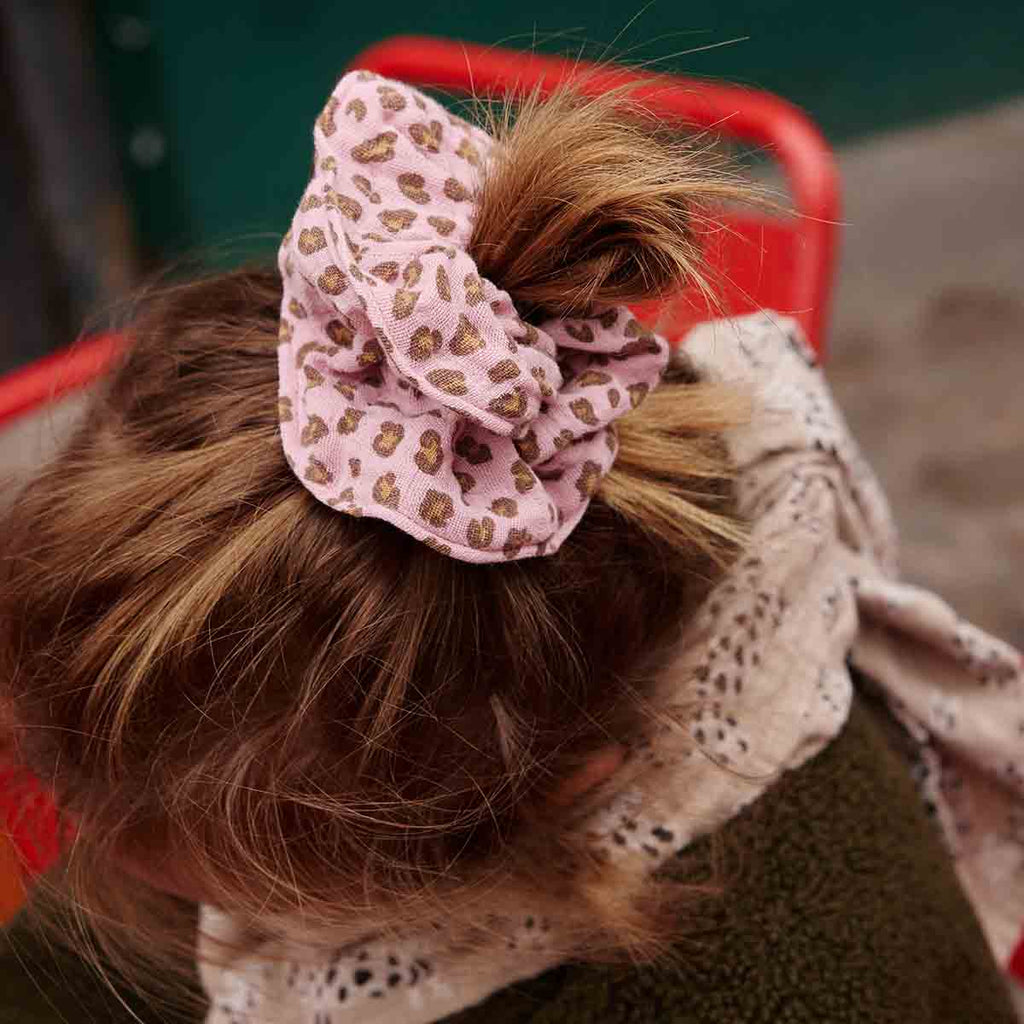 Mini Leopard Candy Pink scrunchie securing a woman's hair in a bun, showcasing its pink muslin fabric and brown leopard print.