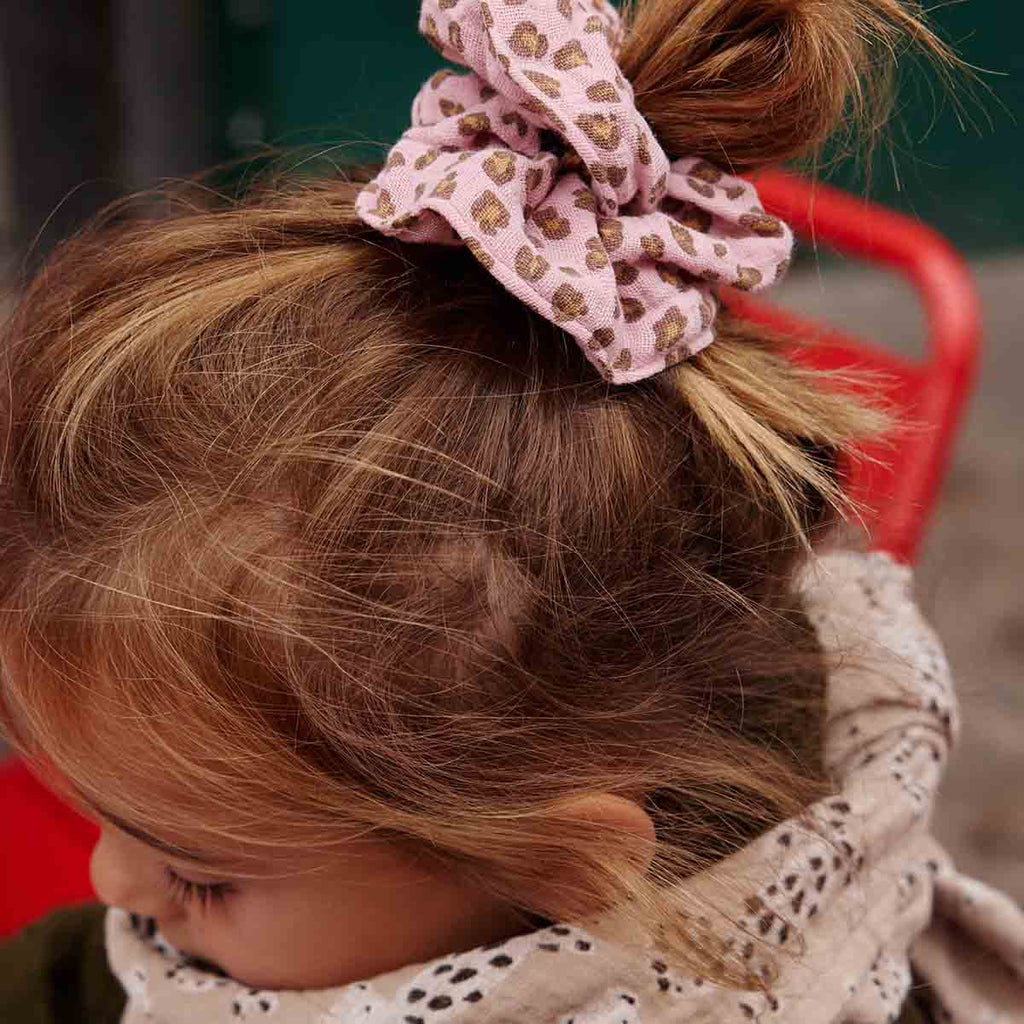 Close-up of a woman wearing the Mini Leopard Candy Pink scrunchie in her hair, highlighting the soft pink fabric and brown leopard pattern.