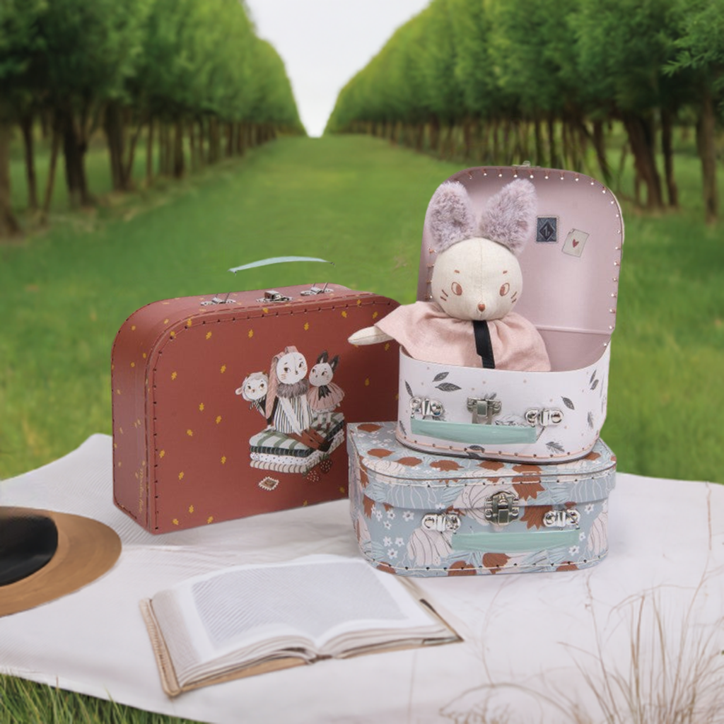 Moulin Roty Après la Pluie set of three decorative storage cases displayed outdoors on a picnic blanket with a rabbit doll inside one case