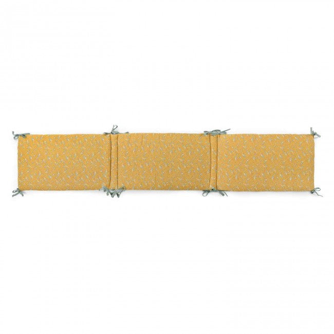 Ochre printed cotton muslin cot bumper laid flat with sage-coloured ties on a white background
