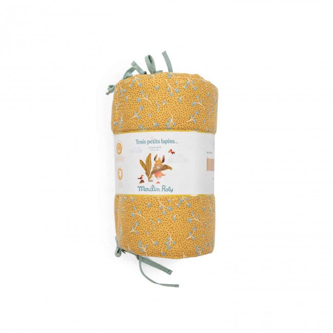 Rolled ochre printed cotton muslin cot bumper with sage-coloured ties and Moulin Roty packaging on a white background