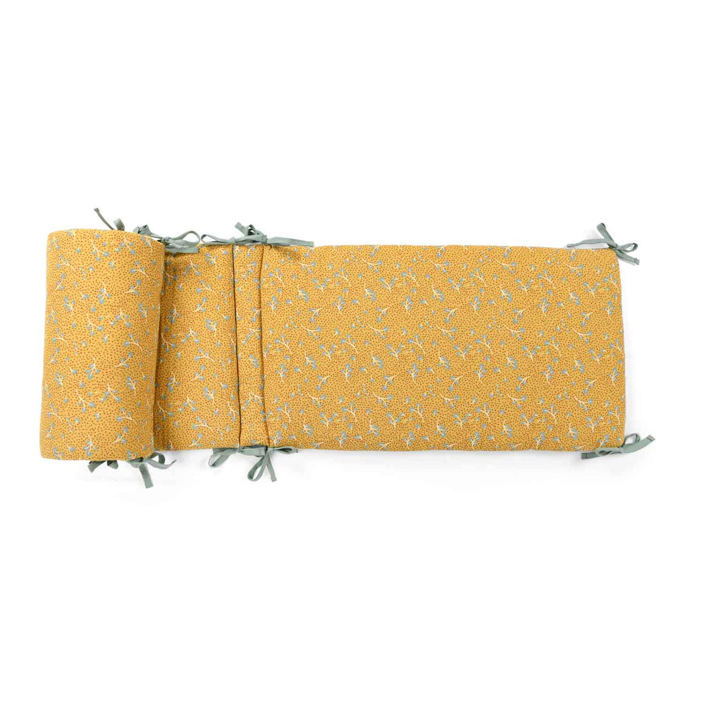 Ochre printed cotton muslin cot bumper with sage-coloured ties displayed on a white background