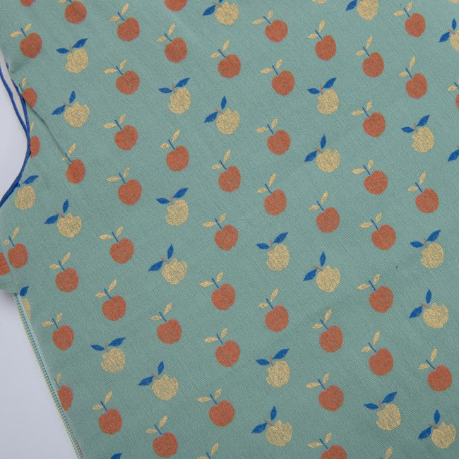 Close-up of the Moulin Roty Pomme des Bois sleeping bag fabric, featuring a blue-green background with repeating rust-orange and yellow apples and small blue leaves.
