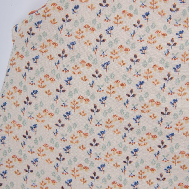 Close-up of the Moulin Roty Woody Apple sleeping bag fabric, featuring a woodland print of colourful leaves, tiny mushrooms, berries and plants on a cream background.