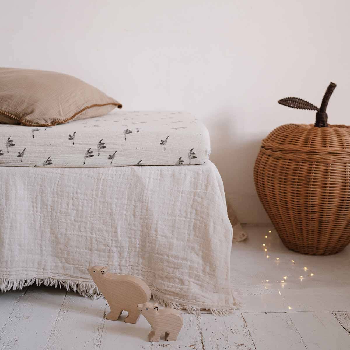 Olivia Goose Natural fitted cot sheet with a delicate grey goose print, styled on a cot with neutral bedding, a woven apple basket and wooden animal toys.